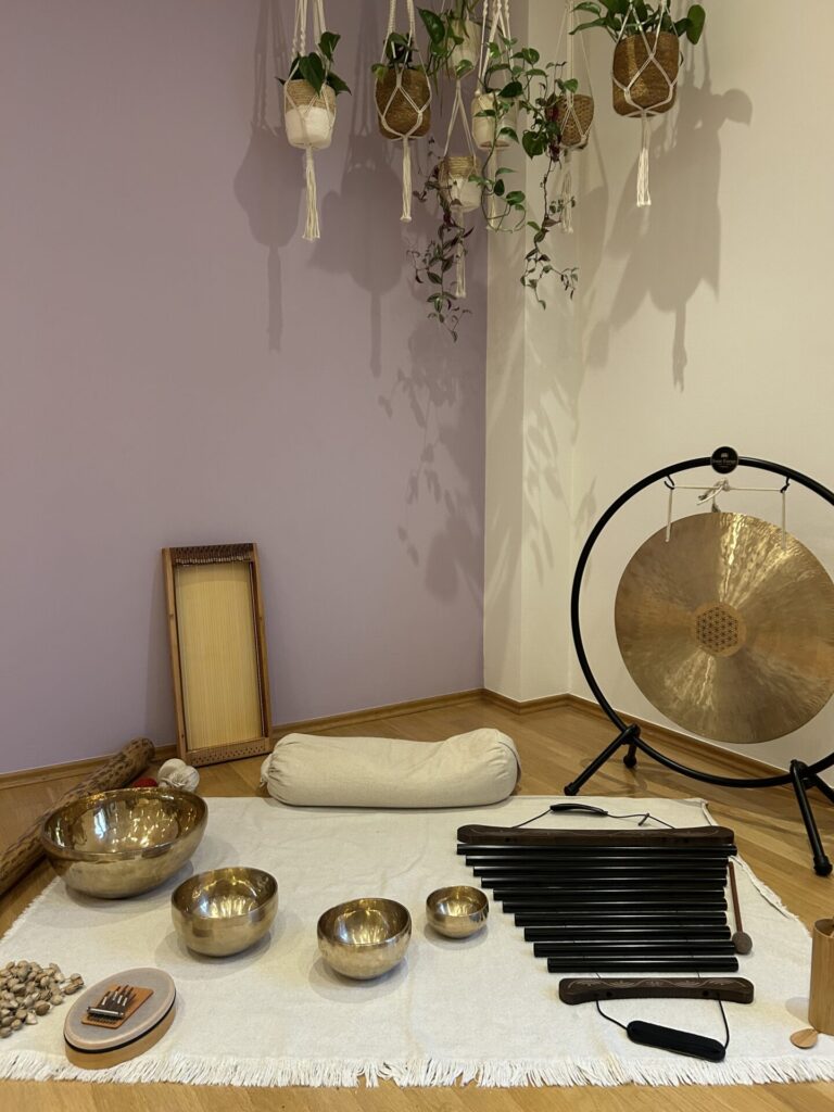 Das Foto zeigt eine Ecke des großen Yogaraums Ganga im Place to be Yoga Studio. Auf dem Boden sind verschiedene Klanginstrumente, wie Klangschalen, Naturinstrumente und ein Gong aufgereiht.