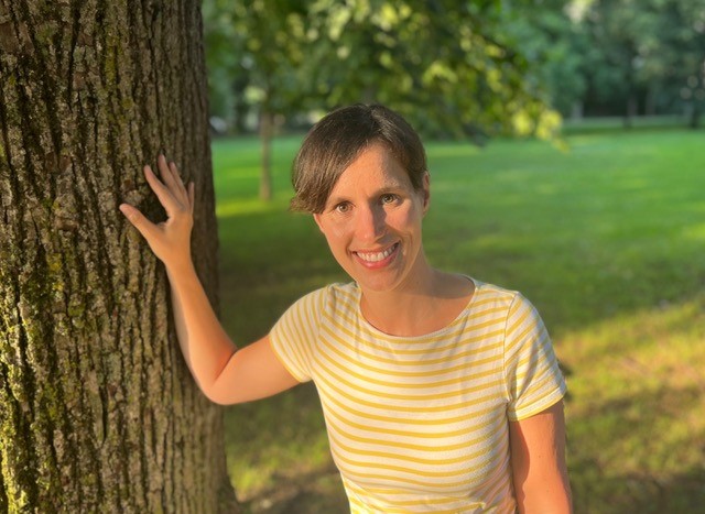 Terea Zölch, eine der Yoga Expertinnen im Place to Be Yogastudio, steht neben einem Baum und blickt freundlich-lächelnd in die Kamera.
